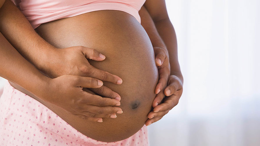 Four arms wrapped around a pregnant woman's belly