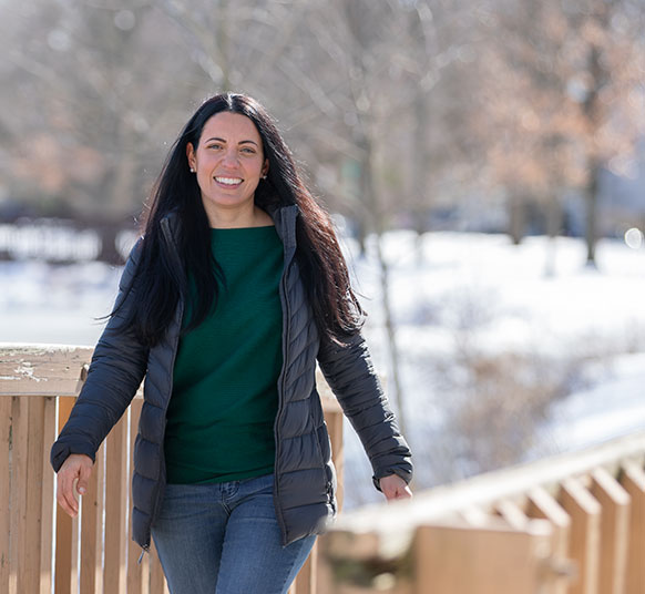 Woman wearing a jacket and jeans walking on a snow covered field with trees background