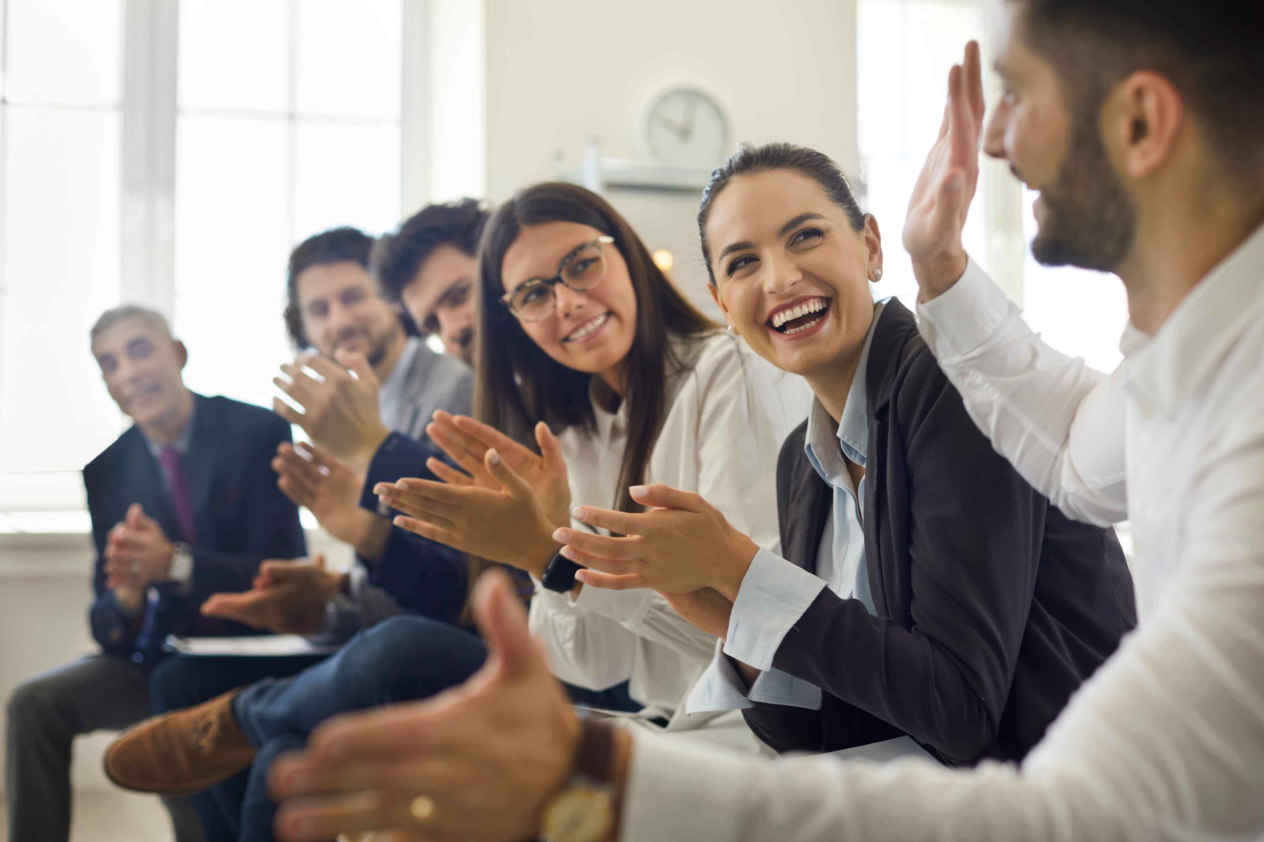 A diverse group of business professionals enthusiastically clapping together in a collaborative environment.