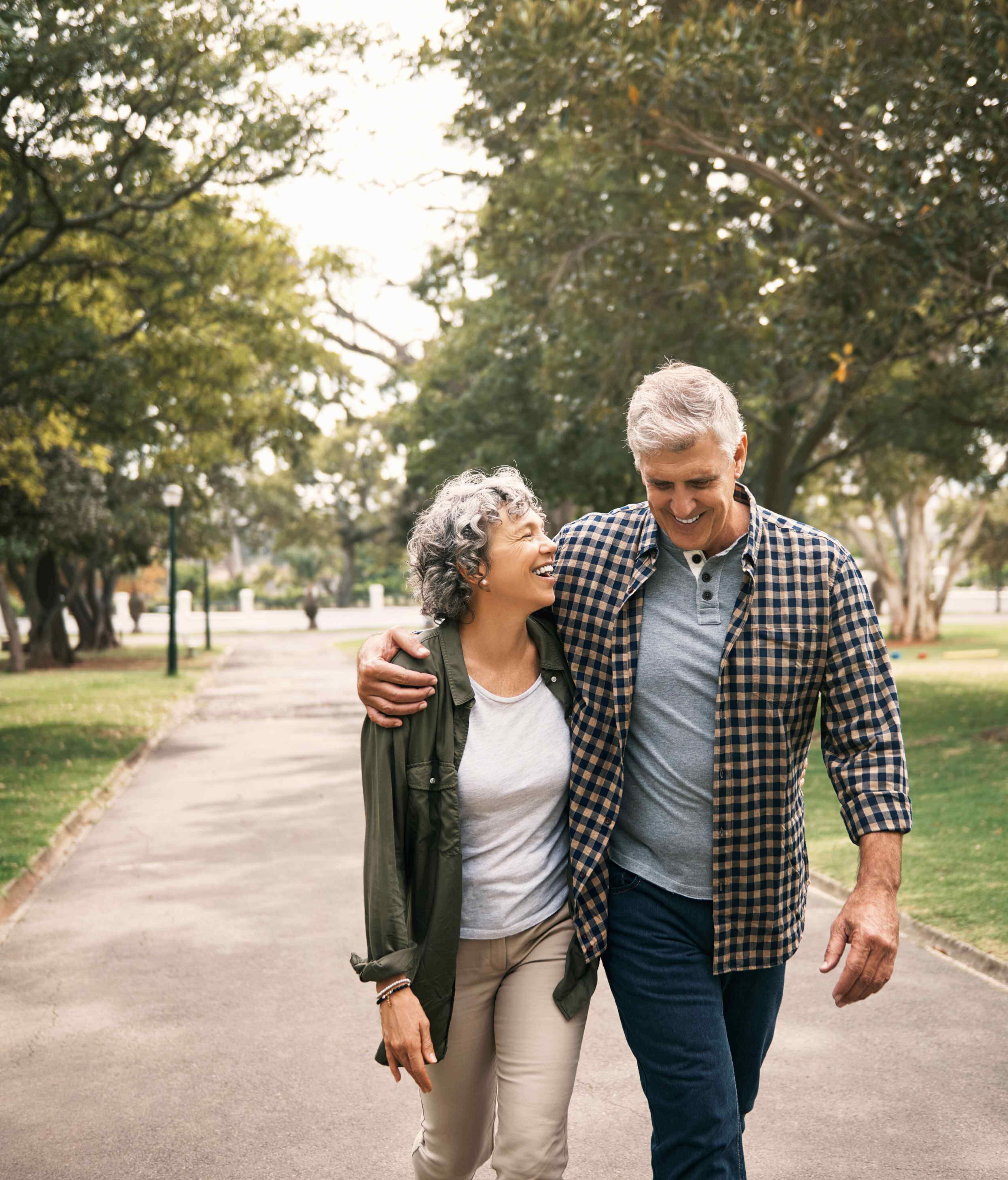 A senior couple strolls hand in hand through a serene park, surrounded by lush greenery and vibrant flowers.