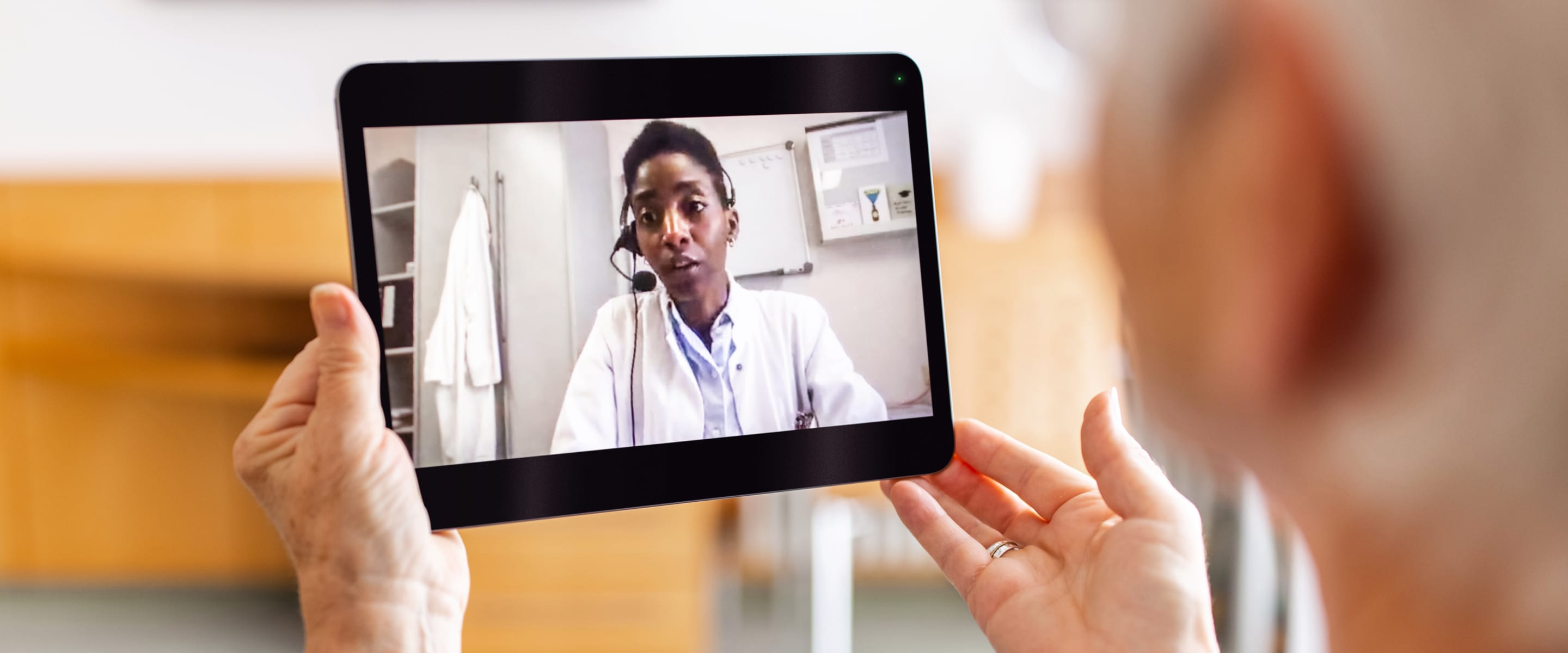 Hands holding a tablet displaying a person wearing a white lab coat with headphones on.