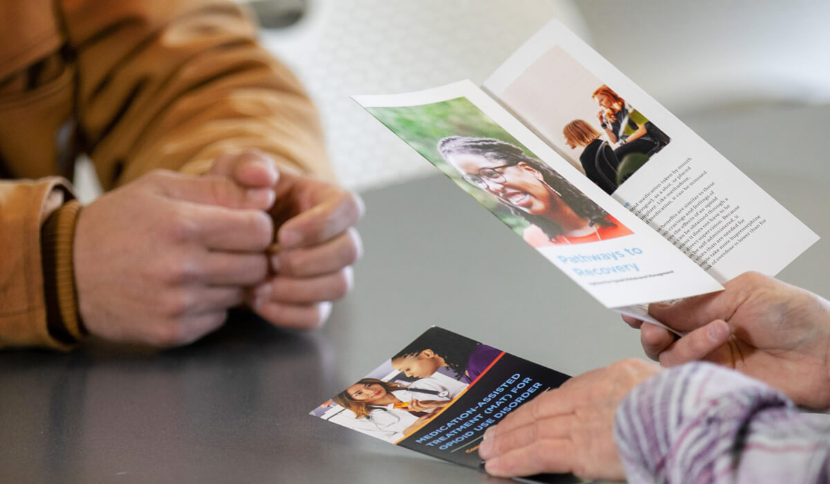 A pair of hands resting on a table with another pair of hands holding brochures