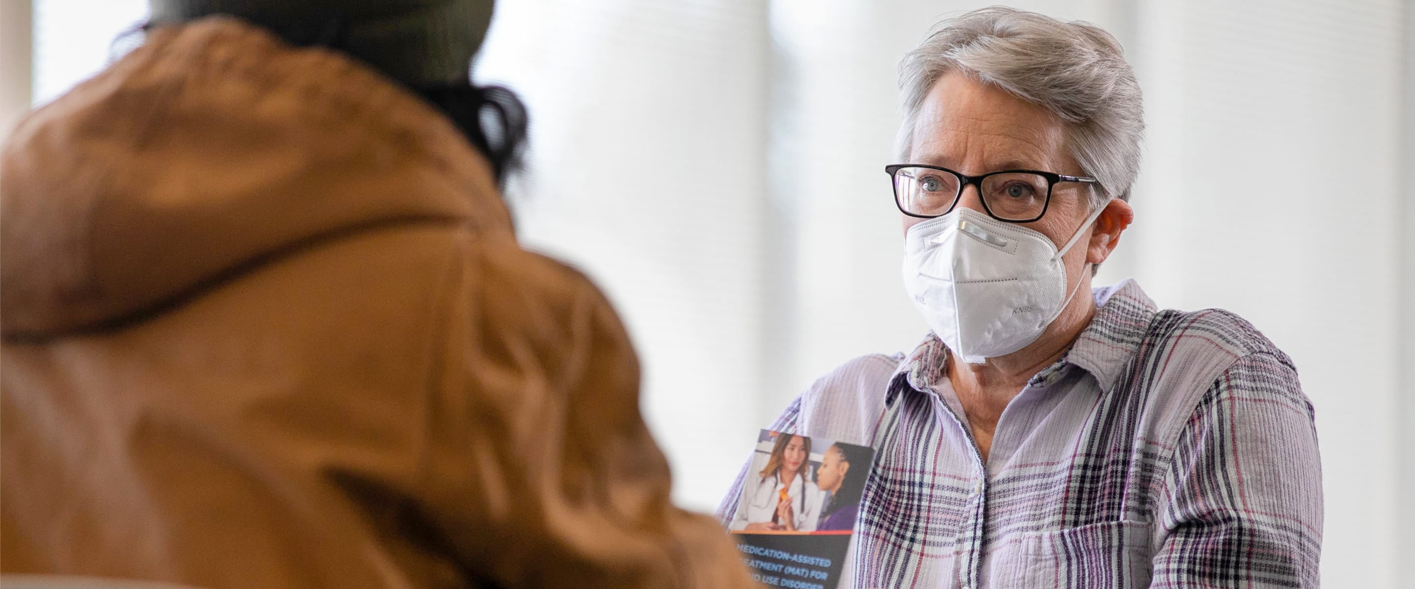 Person with short hair wearing glasses and a white mask looking ahead.